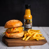 Burger with fries and a bottle of SIAM peanut coconut sauce on a wooden board.