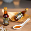 Two bottles of SIAM fish sauce with a spoonful of sauce on a wooden surface.